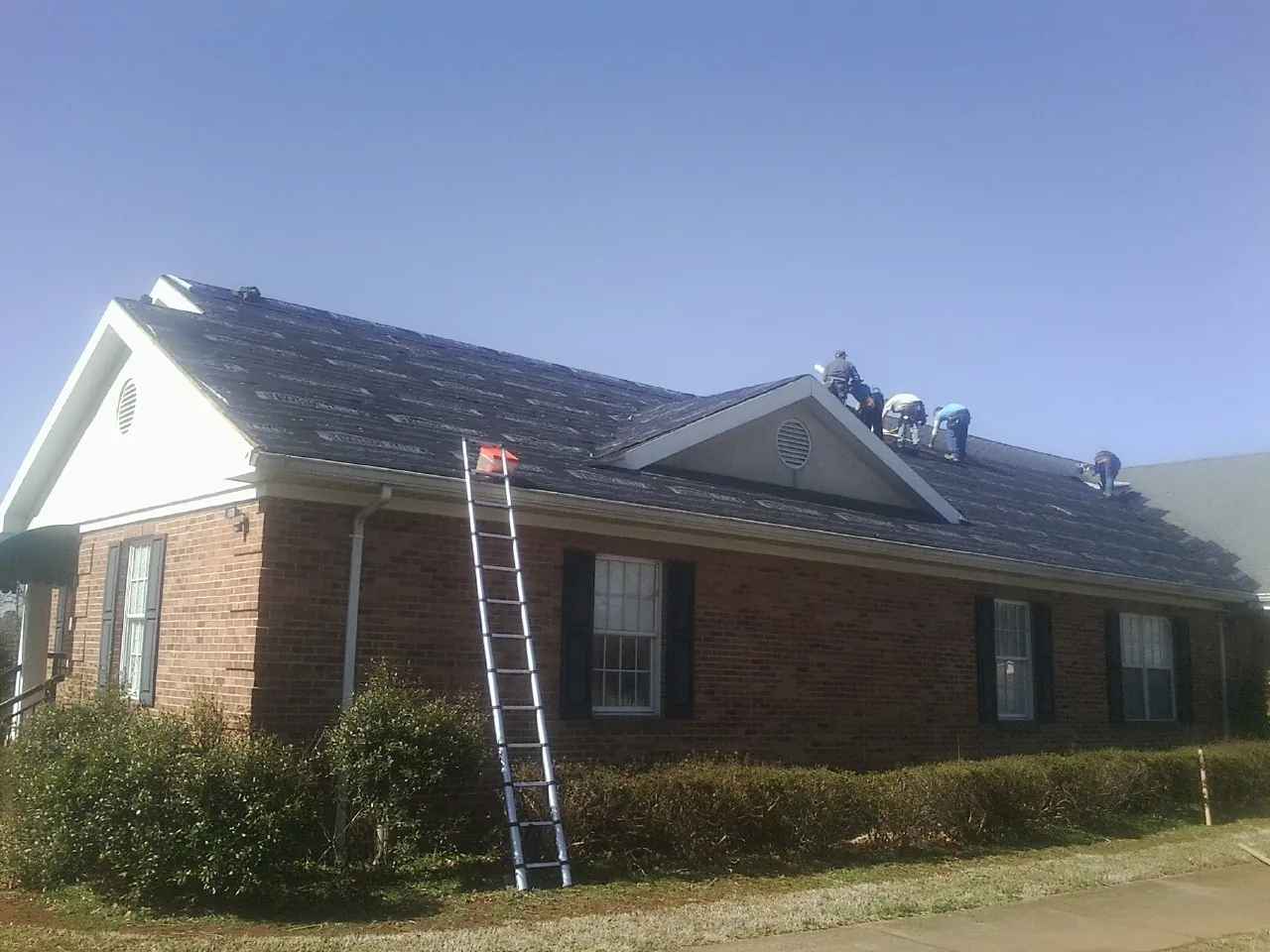 Crew tearing shingles off a brick ranch roof with a ladder set — Metal Roof Repair work by our crew in Neptune