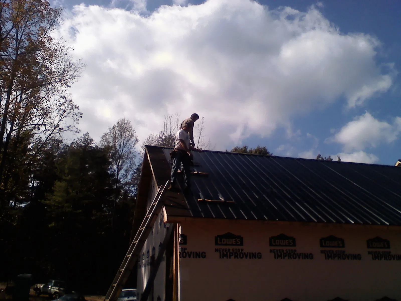 Roofer fastening dark metal panels high against a cloudy sky, from a Roof Inspection job in Neptune
