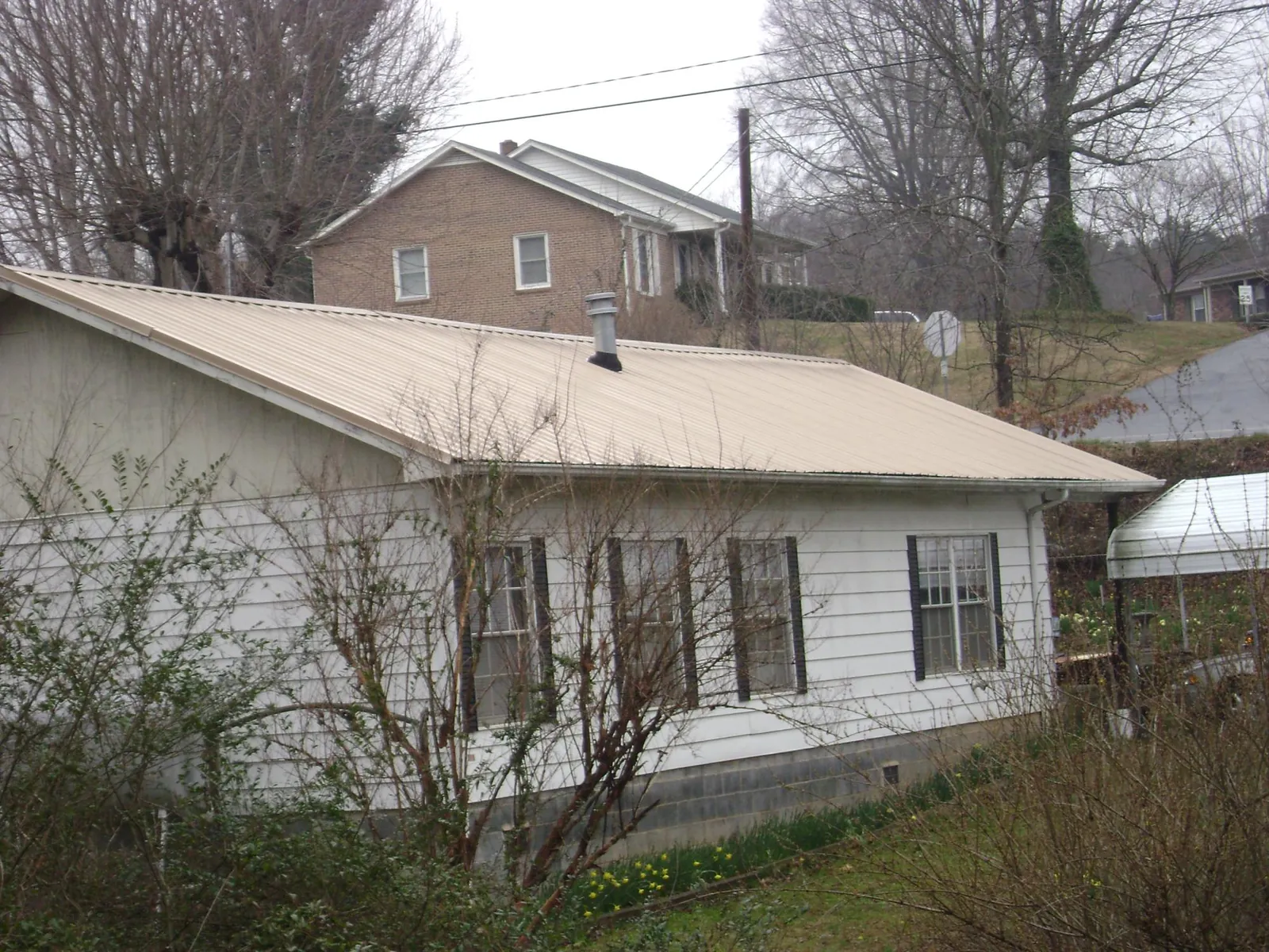 Tan metal roof on a white sided house set into a hillside — Commercial Roofing by Roofing Brothers in Neptune